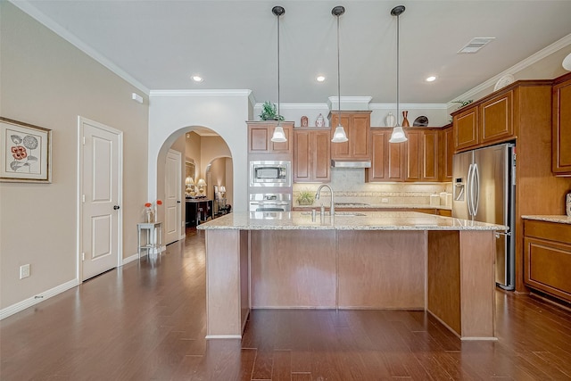 kitchen featuring appliances with stainless steel finishes, decorative light fixtures, tasteful backsplash, a kitchen island with sink, and light stone counters