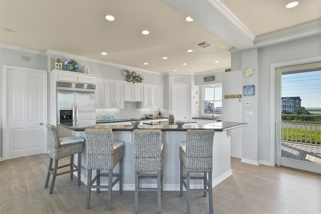 kitchen featuring white cabinetry, stainless steel built in refrigerator, backsplash, a kitchen bar, and light hardwood / wood-style flooring