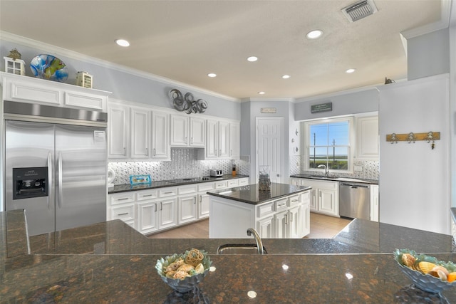 kitchen with white cabinetry, appliances with stainless steel finishes, backsplash, and crown molding