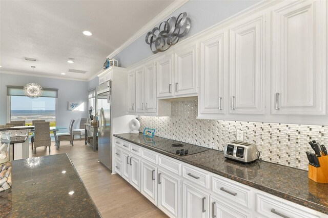 kitchen featuring white cabinetry, hanging light fixtures, dark stone countertops, black electric stovetop, and ornamental molding