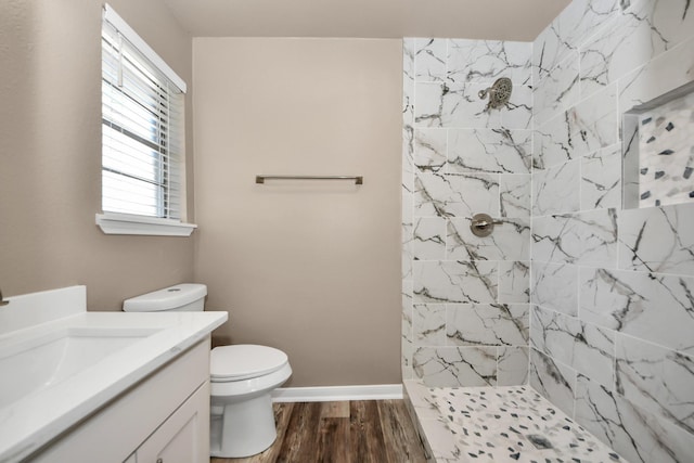 bathroom with wood-type flooring, toilet, vanity, and a tile shower