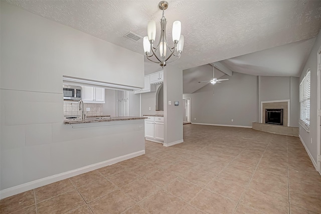 unfurnished living room featuring ceiling fan with notable chandelier, lofted ceiling with beams, a textured ceiling, and light tile patterned floors