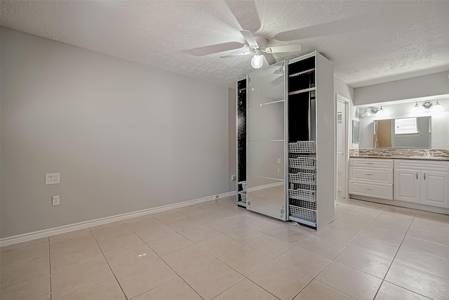 unfurnished bedroom featuring connected bathroom, sink, a textured ceiling, light tile patterned floors, and ceiling fan