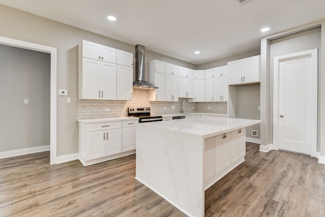 kitchen with white cabinetry, a center island, electric range, light wood-type flooring, and wall chimney exhaust hood