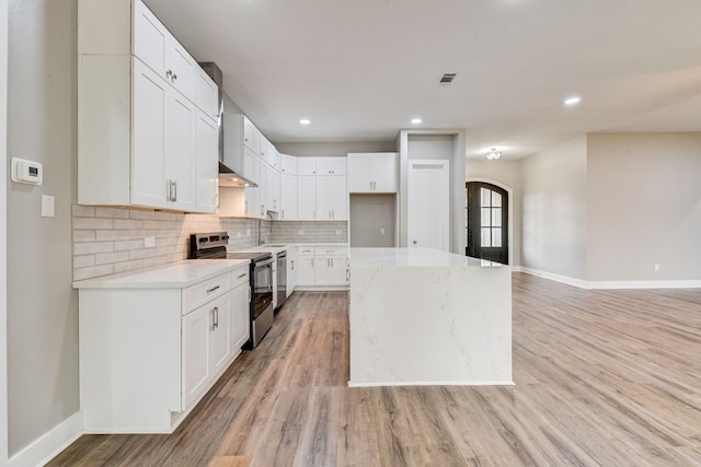 kitchen with white cabinetry, backsplash, a center island, wall chimney range hood, and electric stove