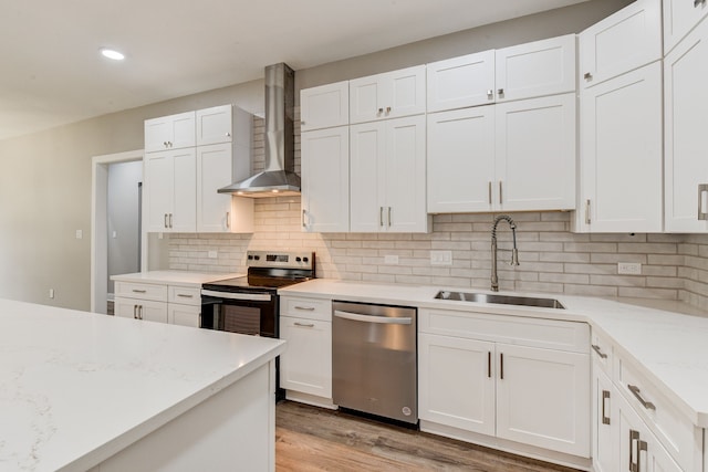 kitchen with appliances with stainless steel finishes, white cabinetry, sink, light hardwood / wood-style floors, and wall chimney range hood