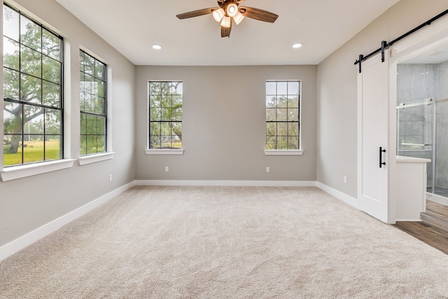 empty room featuring ceiling fan, a barn door, and carpet floors