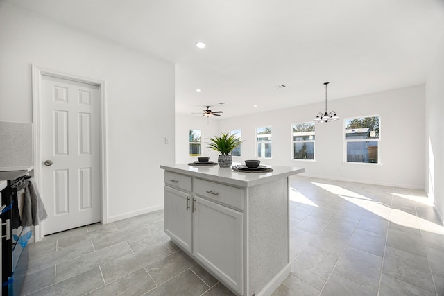 kitchen featuring white cabinetry, a center island, hanging light fixtures, light tile patterned floors, and ceiling fan with notable chandelier