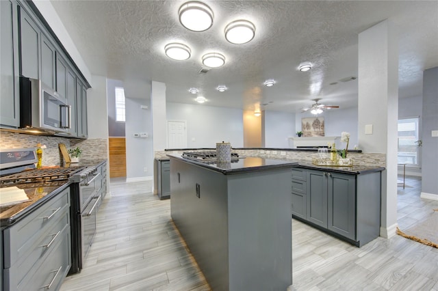 kitchen featuring gray cabinets, a kitchen island, appliances with stainless steel finishes, decorative backsplash, and kitchen peninsula