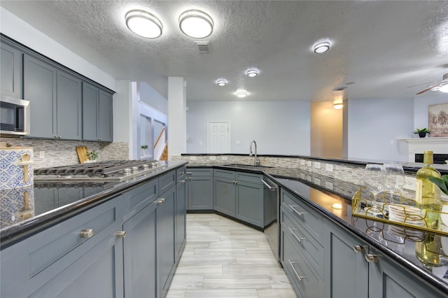 kitchen featuring appliances with stainless steel finishes, sink, gray cabinetry, decorative backsplash, and dark stone counters