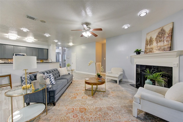 living room with ceiling fan, a high end fireplace, a textured ceiling, and light hardwood / wood-style floors