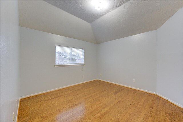 unfurnished room with vaulted ceiling, a textured ceiling, and light wood-type flooring