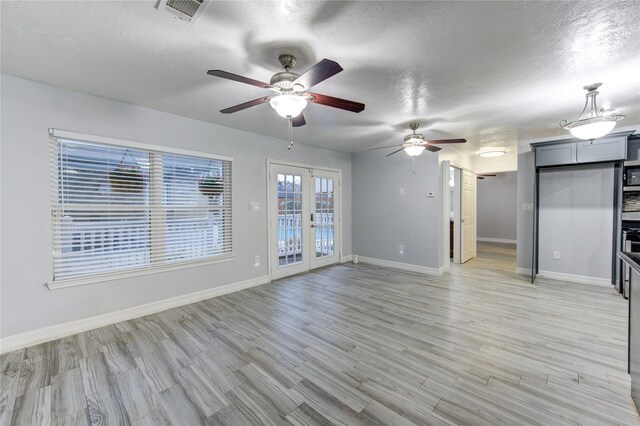 unfurnished living room with ceiling fan, light hardwood / wood-style flooring, a textured ceiling, and french doors