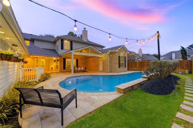 pool at dusk with a fenced backyard, a ceiling fan, a yard, a fenced in pool, and a patio area