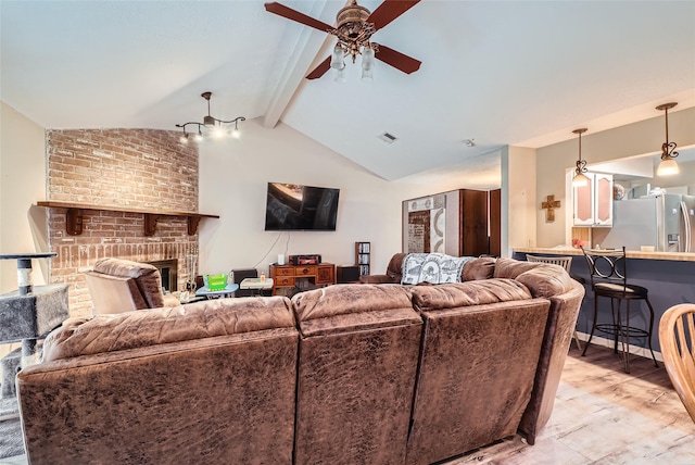 living room with ceiling fan, vaulted ceiling with beams, a fireplace, and light hardwood / wood-style floors