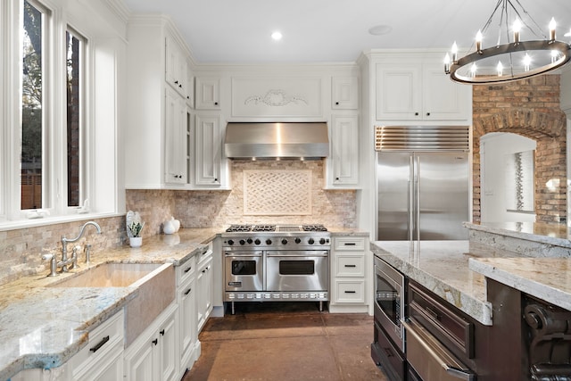 kitchen with pendant lighting, white cabinetry, built in appliances, ventilation hood, and light stone countertops