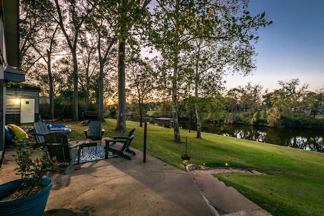 patio terrace at dusk featuring a water view and a yard