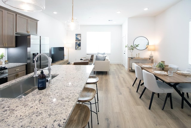 kitchen featuring decorative light fixtures, light stone countertops, sink, and light wood-type flooring