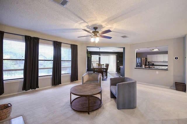 living room featuring ceiling fan, light colored carpet, and a textured ceiling