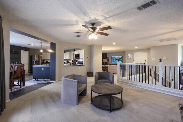 living area with light carpet, ceiling fan, and a textured ceiling