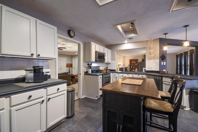 kitchen with pendant lighting, appliances with stainless steel finishes, a kitchen breakfast bar, white cabinets, and kitchen peninsula