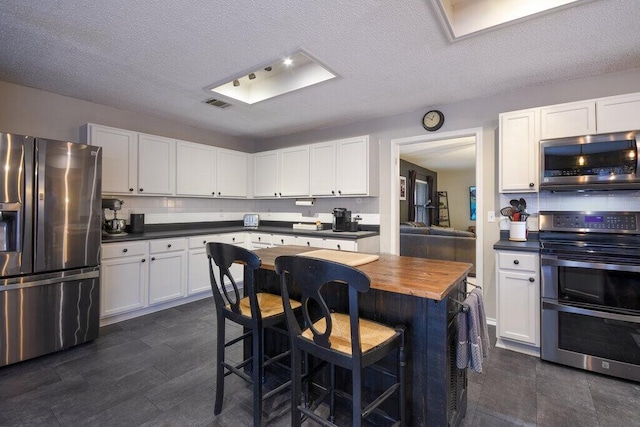 kitchen with butcher block counters, a breakfast bar, stainless steel appliances, decorative backsplash, and white cabinets