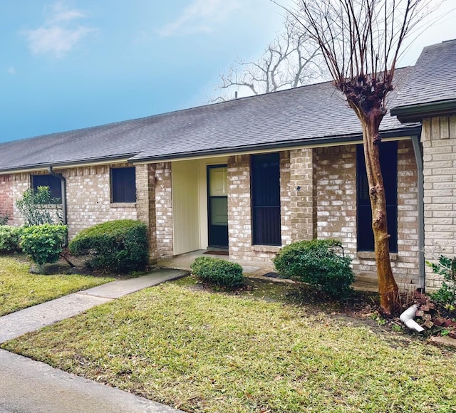 ranch-style house featuring brick siding, a front yard, and a shingled roof