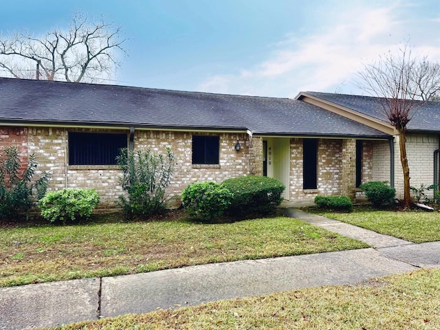 view of front facade featuring a front lawn, roof with shingles, and brick siding