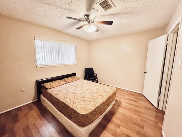 bedroom with light wood-type flooring, visible vents, ceiling fan, and a textured ceiling