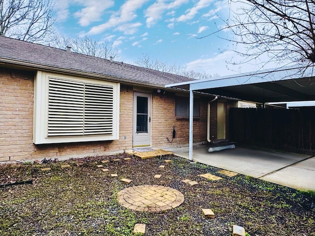 property entrance featuring a shingled roof, brick siding, fence, and a carport