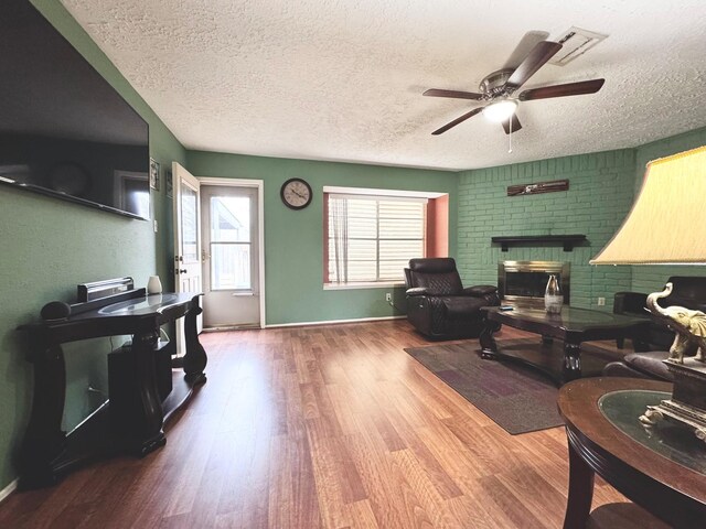 living room featuring a brick fireplace, wood-type flooring, a textured ceiling, and ceiling fan