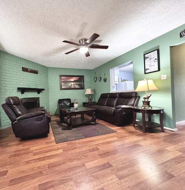 living room with baseboards, a ceiling fan, wood finished floors, a textured ceiling, and a fireplace