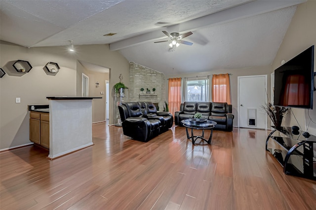 living room with ceiling fan, lofted ceiling with beams, a textured ceiling, and light wood-type flooring