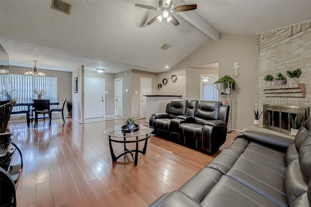 living room featuring vaulted ceiling with beams, wood-type flooring, a fireplace, a textured ceiling, and ceiling fan with notable chandelier