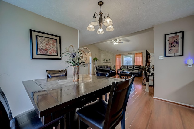 dining room featuring hardwood / wood-style flooring, vaulted ceiling, a textured ceiling, and ceiling fan with notable chandelier