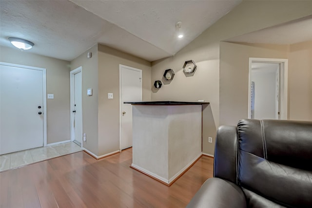 entrance foyer featuring light hardwood / wood-style flooring, a textured ceiling, and vaulted ceiling