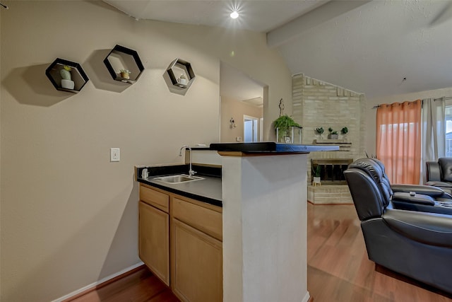 kitchen with light brown cabinetry, sink, vaulted ceiling with beams, light wood-type flooring, and kitchen peninsula