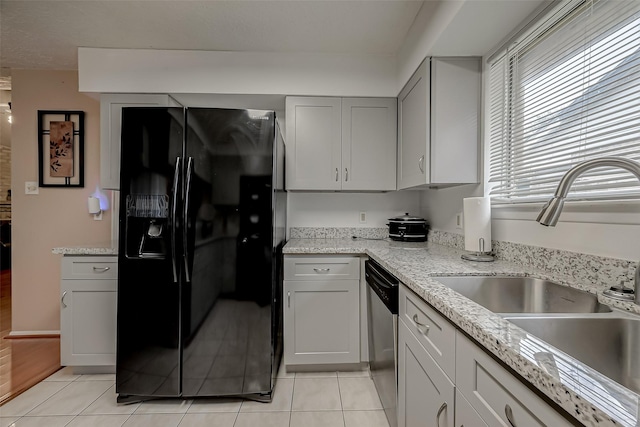 kitchen with sink, black fridge, light stone counters, light tile patterned floors, and stainless steel dishwasher