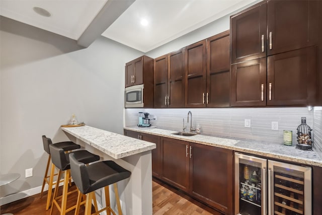 kitchen featuring wine cooler, a kitchen bar, light stone counters, stainless steel microwave, and backsplash