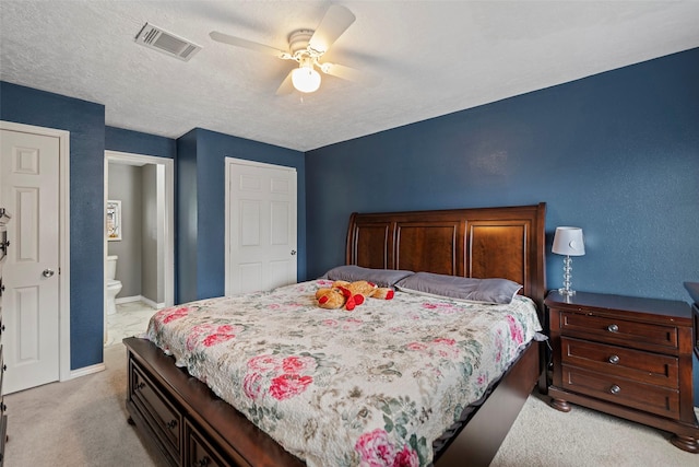 bedroom featuring ceiling fan, ensuite bath, light carpet, and a textured ceiling