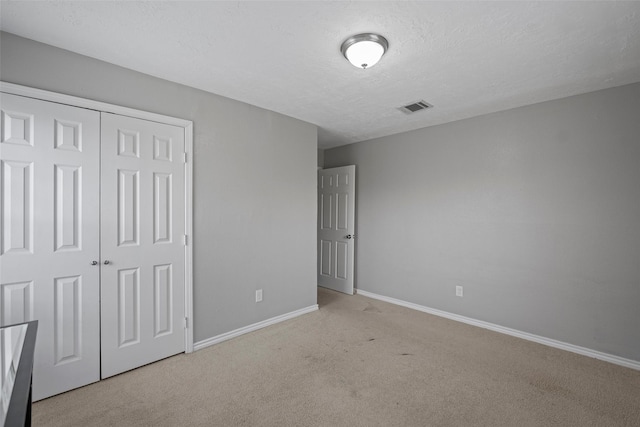 unfurnished bedroom with light colored carpet, a closet, and a textured ceiling