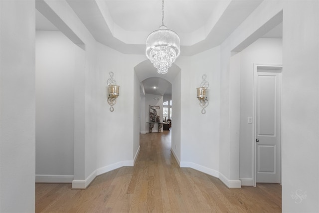 hall featuring a raised ceiling, an inviting chandelier, and light hardwood / wood-style flooring