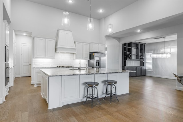 kitchen with white cabinetry, a kitchen island with sink, stainless steel appliances, custom range hood, and stone countertops