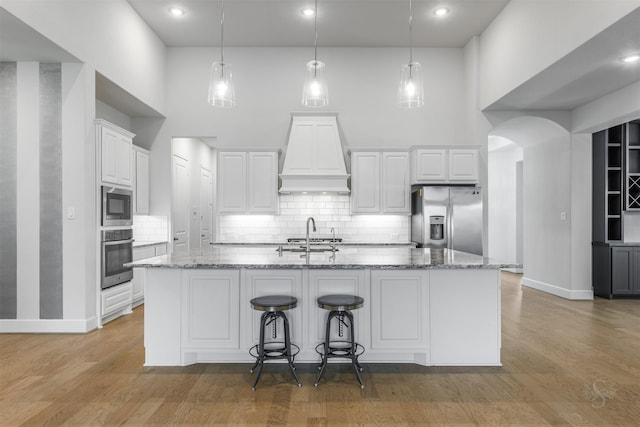 kitchen with white cabinetry, appliances with stainless steel finishes, a center island with sink, and light stone counters