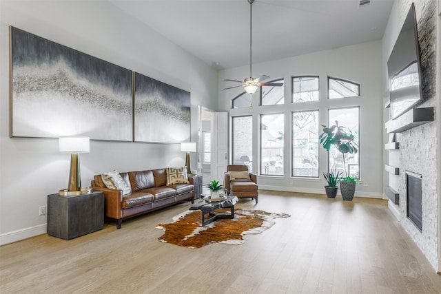 living room featuring ceiling fan, a fireplace, a high ceiling, and light wood-type flooring