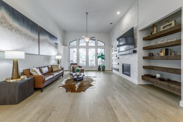 living room featuring built in shelves, a stone fireplace, a high ceiling, and light wood-type flooring