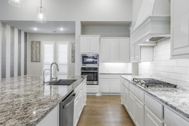 kitchen with pendant lighting, custom range hood, white cabinets, and appliances with stainless steel finishes