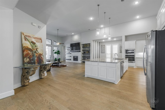 kitchen with sink, white cabinetry, a center island with sink, stainless steel appliances, and light stone countertops