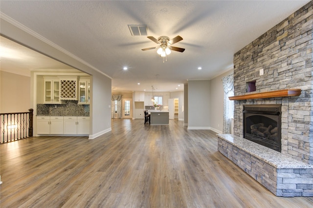 unfurnished living room with hardwood / wood-style flooring, crown molding, ceiling fan, and a fireplace