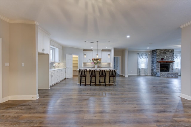 kitchen with pendant lighting, a breakfast bar area, white cabinets, dark wood-type flooring, and a center island with sink